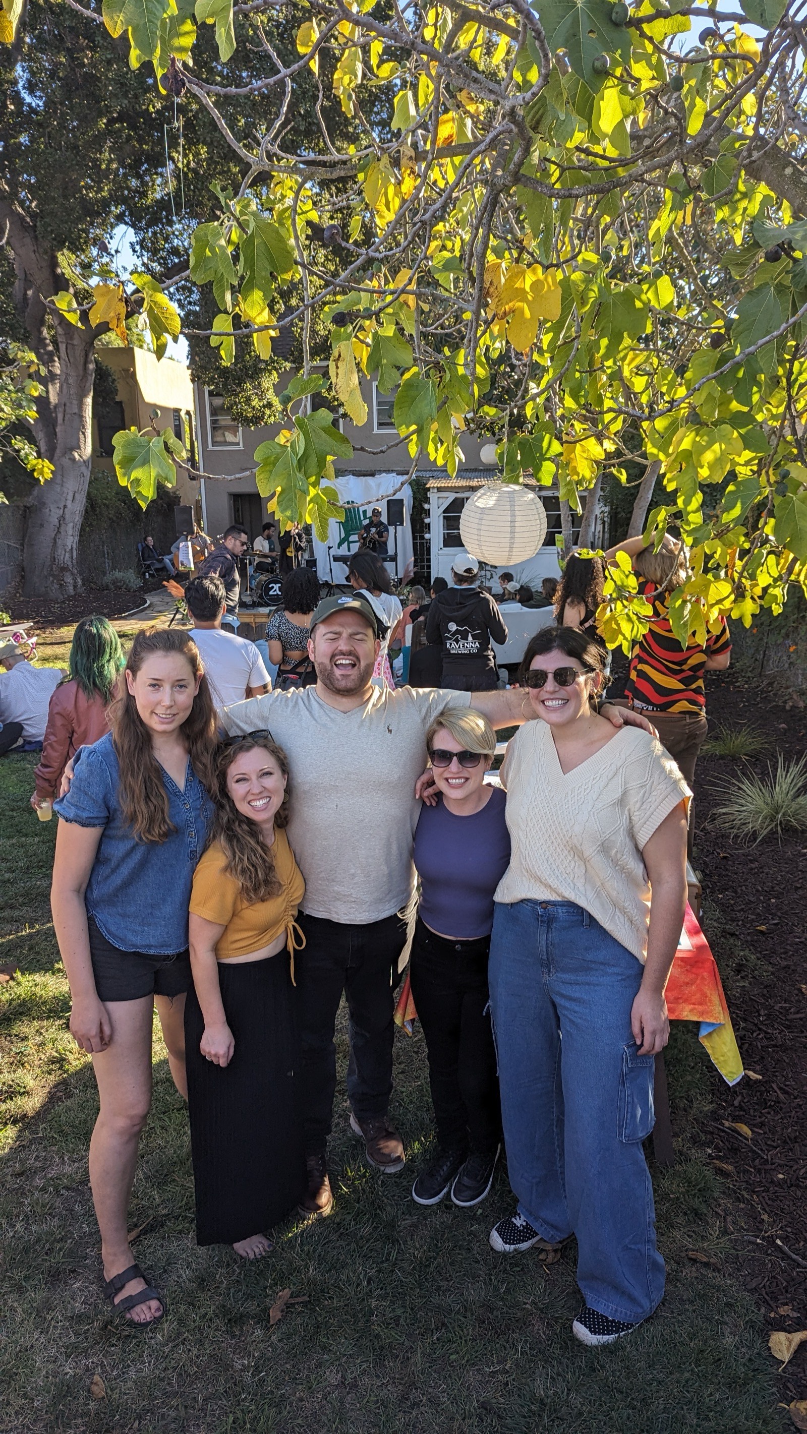 A group of friends laughing together under a tree, 2023