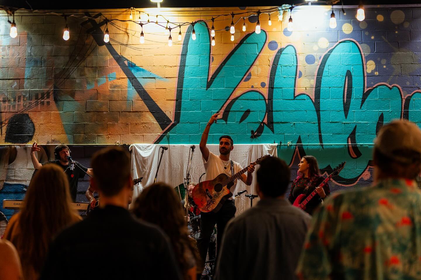 A band performing in front of a colorful mural wall